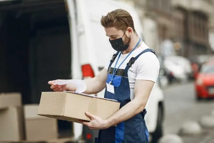 Homem com caixa na mão, conferindo dados de entrega.